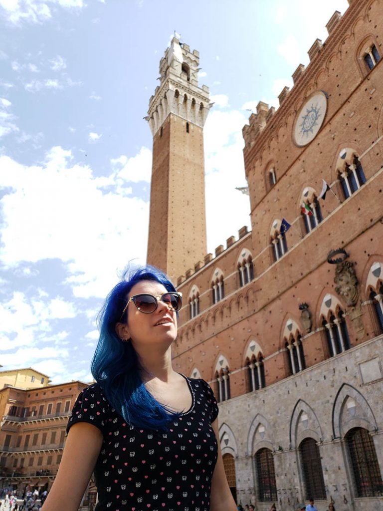 mulher de cabelo azul em frente ao palacio publico e torre mangia em siena