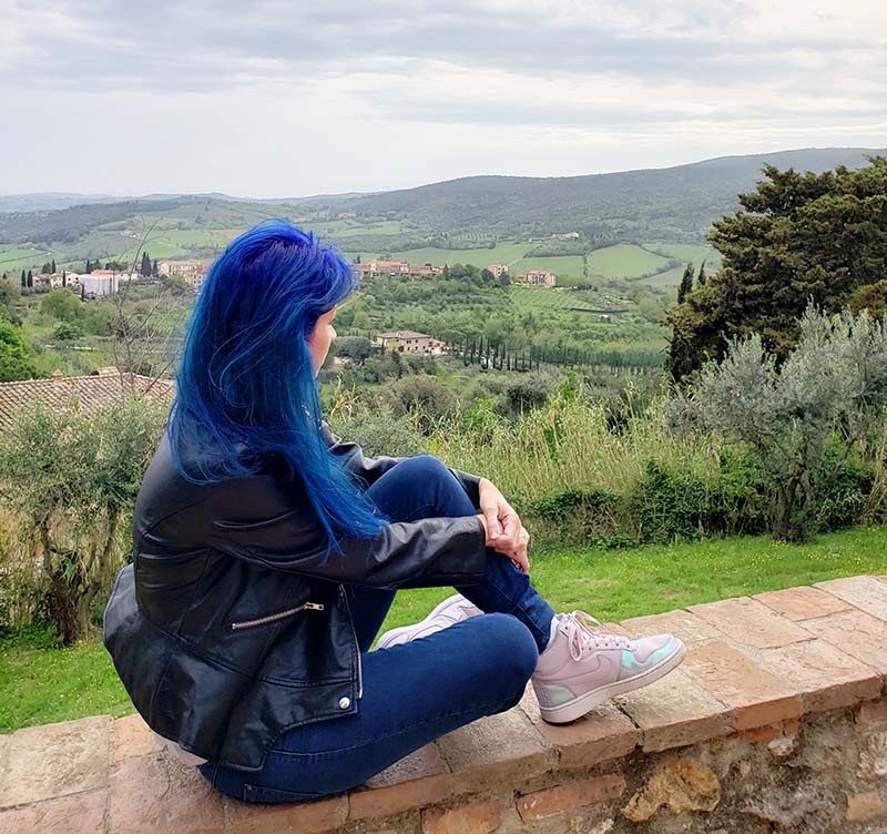mulher de cabelo azul olhando para vinhedos em san gimignano toscana