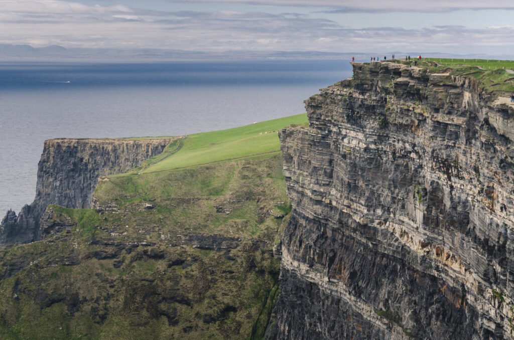 Vista panorâmica dos Cliffs of Moher na Irlanda, com falésias imponentes e turistas apreciando a paisagem, exemplo de roteiro slow travel na Europa