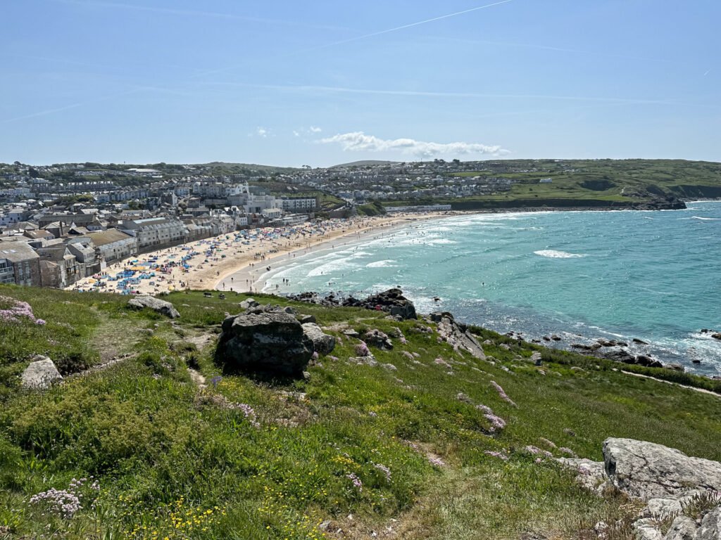Vista panorâmica da praia de Porthmeor em St. Ives, Cornualha, com mar azul e casas à beira-mar, destaque de uma road trip costeira pela Inglaterra