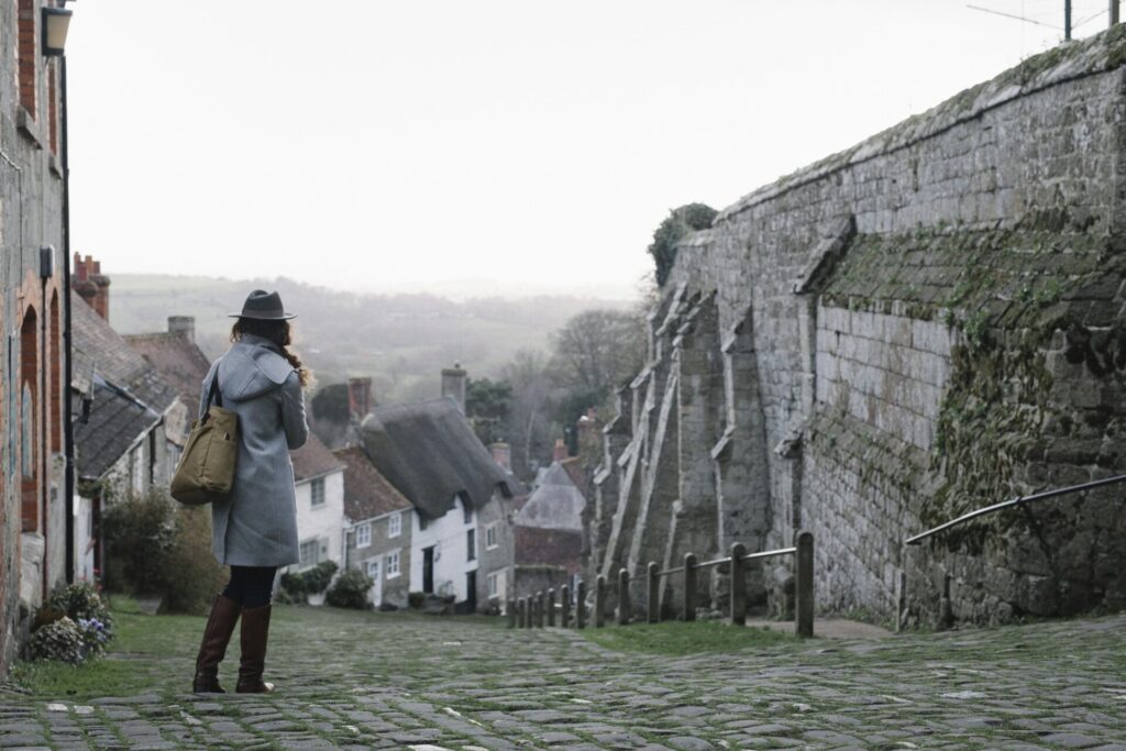 Pessoa caminhando por uma rua de pedra em um vilarejo medieval da Escócia, cercada por casas antigas e muralhas históricas