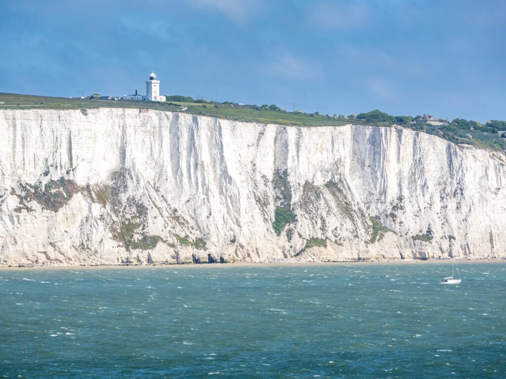 Vista das White Cliffs of Dover com farol no topo e mar azul, ponto turístico imperdível em uma road trip pela Inglaterra