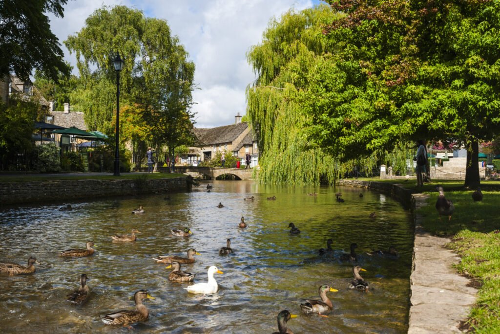 Vista de Bourton-on-the-Water com rio, patos e casas de pedra típicas dos Cotswolds, rota clássica de road trip pela Inglaterra