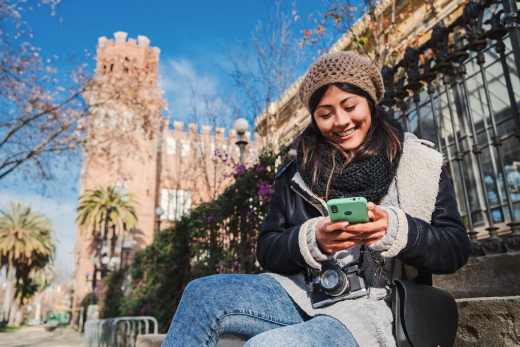 Mulher viajante sorrindo enquanto usa aplicativo de comunicação no celular durante viagem pela Europa
