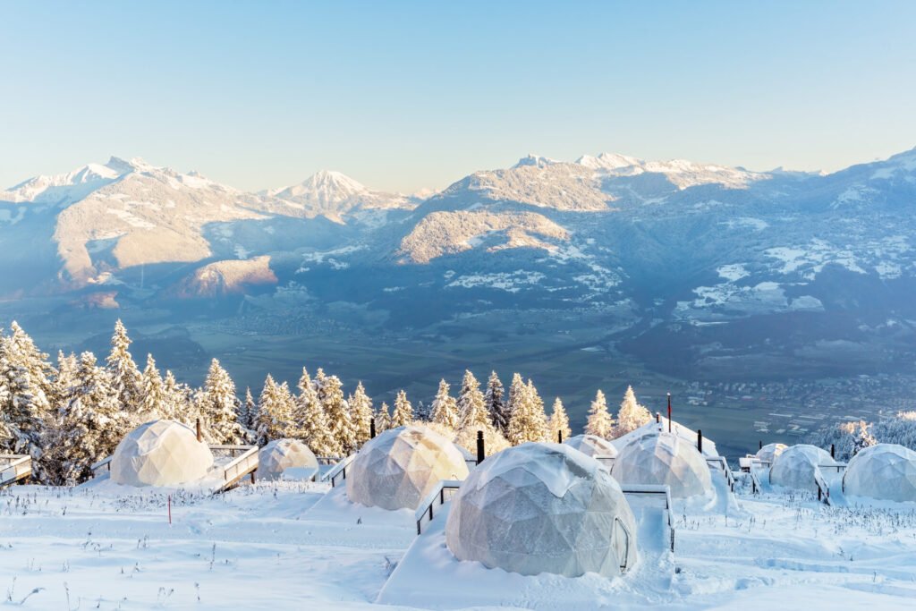 Vista das cabanas em formato de iglu do hotel Whitepod cobertas de neve nas montanhas da Suíça durante o inverno europeu