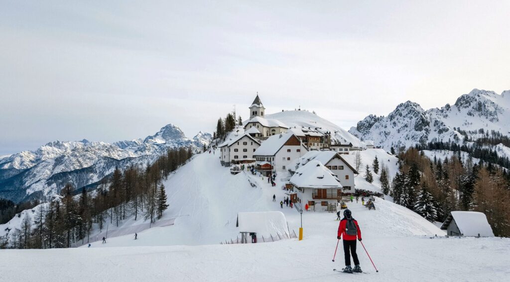 Pessoa esquiando em Monte Lussari, Itália, com vilarejo e montanhas cobertas de neve ao fundo durante o inverno europeu