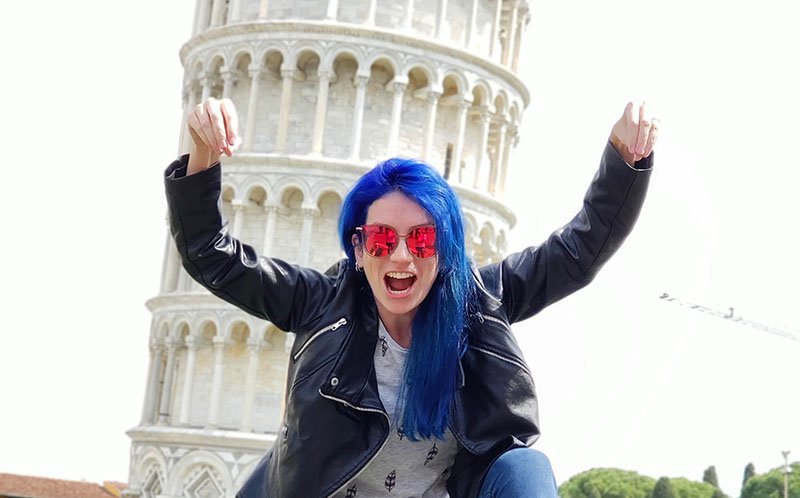 mulher de cabelo azul fazendo pose de luta em frente a torre inclinada