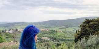 Roteiro na Toscana: o que fazer em 8 dias e dicas de viagem mulher de cabelo azul olhando para vinhedos em san gimignano toscana